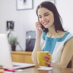 Lady working from home holding mug talking on phone 1