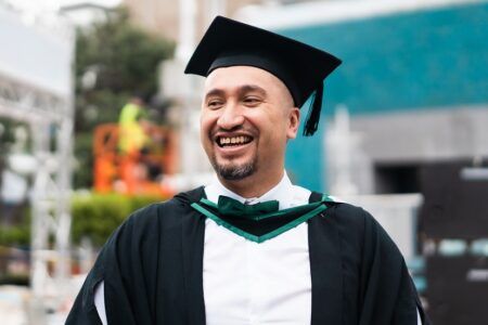 Male student in graduation cap and gown outside smiling